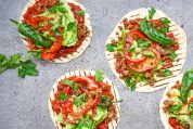 Vier ungerollte Tortillas mit Tomatensosse, Pepperoni, Kräutern und Fleisch belegt Vier ungerollte Tortillas mit Tomatensosse, Pepperoni, Kräutern und Fleisch belegt